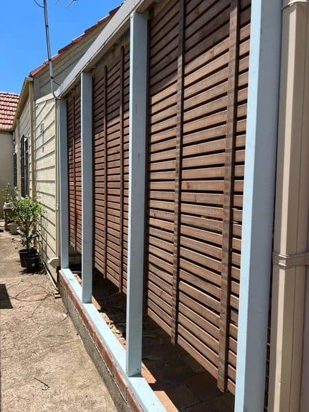 Hardwood slat privacy screens on white posts along the side of a Mascot house