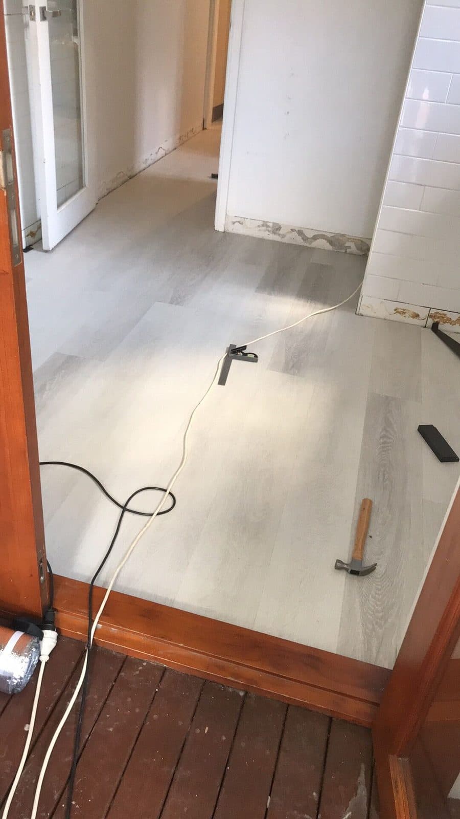 Grey timber-look laminate being laid through a hallway, tools on the floor